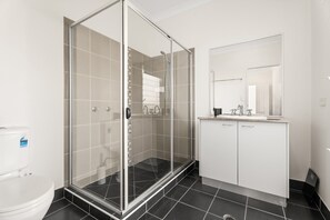A modern bathroom with a glass-enclosed shower, a white toilet, and a vanity with a mirror. - Coastal 4-bed Retreat With Pool in Toogoom (Toogoom)