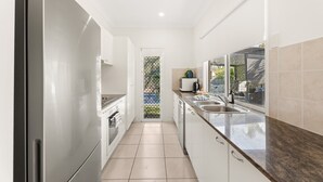 Una cocina estrecha con armarios blancos, un refrigerador de acero inoxidable, un ventanal con vistas y una puerta que da al exterior.