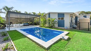 Un patio trasero con piscina, un porche cubierto y una casa de diseño moderno.
