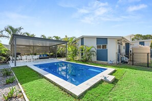 A backyard with a swimming pool, a covered patio, and a house with a modern design. - Coastal 4-bed Retreat With Pool in Toogoom (Toogoom)