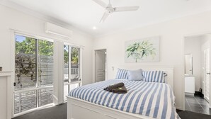 Un dormitorio con una cama grande, un ventilador de techo, una ventana con persianas y una puerta que da a otra habitación.