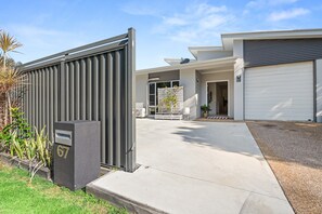 A modern house with a gated driveway, a garage, and a well-maintained lawn. - Coastal 4-bed Retreat With Pool in Toogoom (Toogoom)