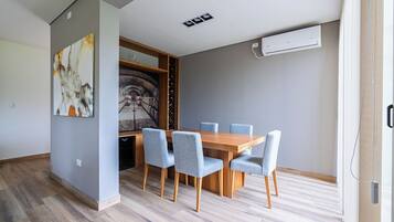 A dining area with a wooden table and four chairs, a wine rack, and a painting on the wall.