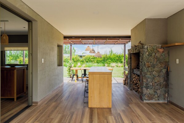 A modern kitchen with a stone fireplace, a wooden dining table, and a view of the garden. - MOT Tupungato Entrevides (Tupungato)