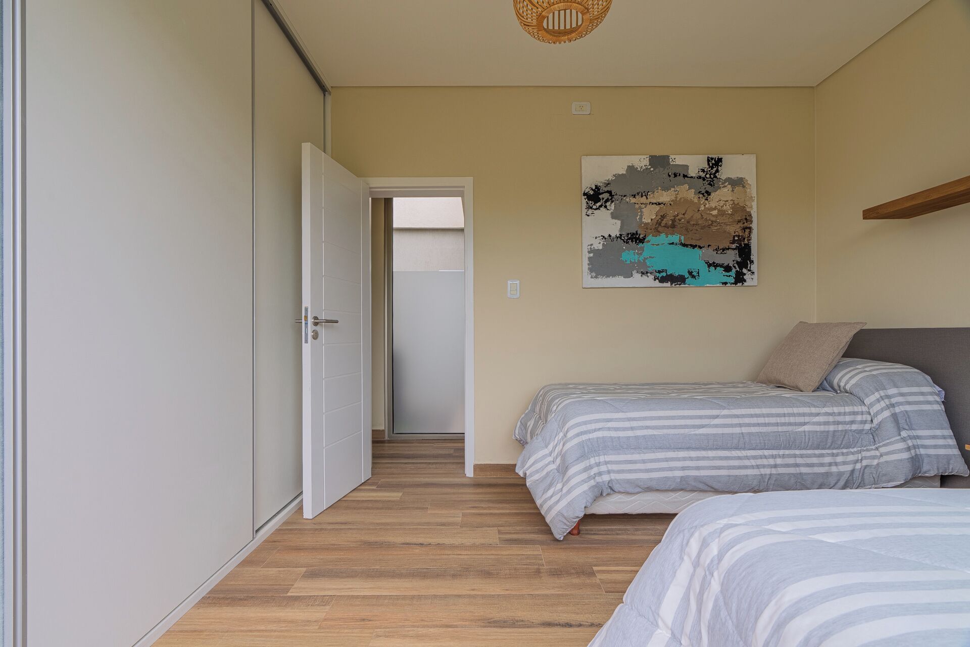 A bedroom with a bed, a door, a wall with a painting, and a wooden floor.
