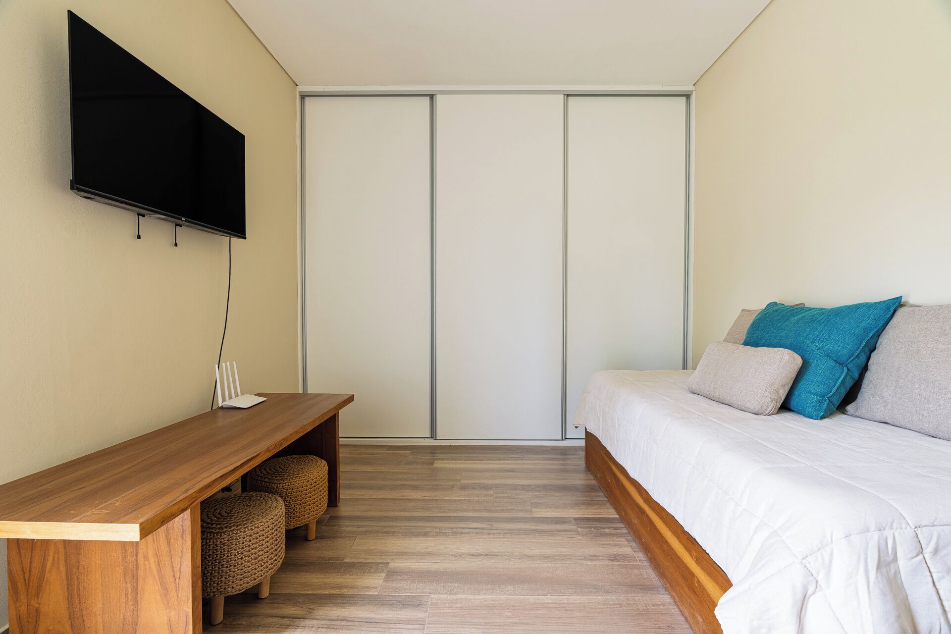 A bedroom with a bed, a TV mounted on the wall, a wooden bench, and a wardrobe.