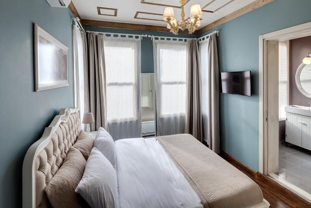 Una camera da letto con un letto, tende, una TV e un bagno parzialmente visibile attraverso una porta aperta.