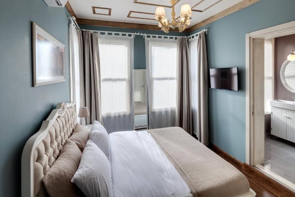 Una camera da letto con un letto, tende, una TV e un bagno parzialmente visibile attraverso una porta aperta.