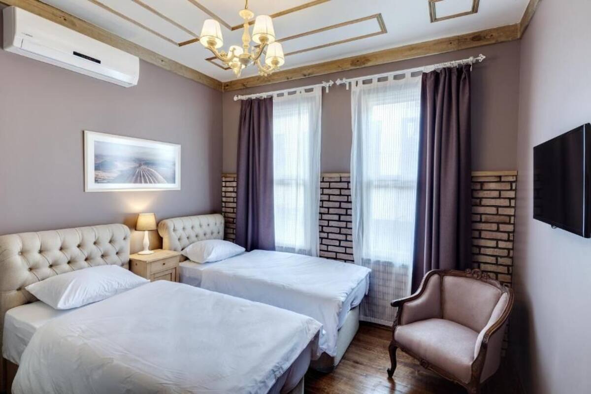 Una camera d'albergo con due letti, una poltrona, una televisione, un lampadario e un quadro appeso al muro.