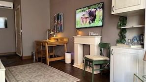 Un salon confortable avec une cheminée, un téléviseur, un bureau et un fauteuil vert.