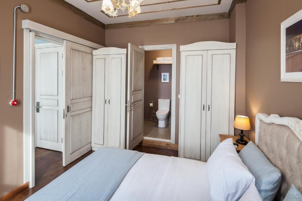 Una camera da letto con un letto, un comodino con una lampada e vista su un bagno attraverso una porta aperta.