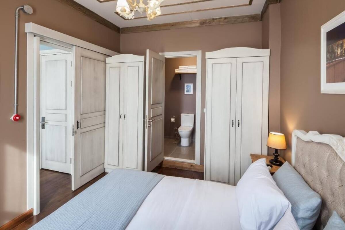 Una camera da letto con un letto, un comodino con una lampada e vista su un bagno attraverso una porta aperta.