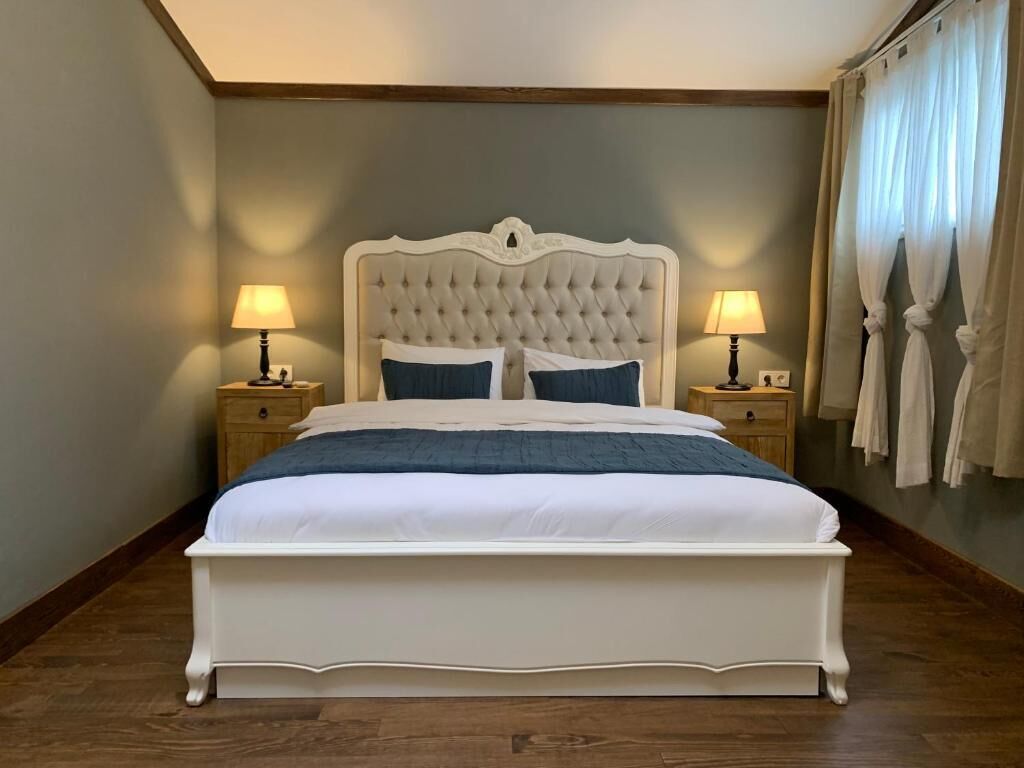 Un letto grande con testiera trapuntata, due lampade ai lati del letto e vista del pavimento in legno della stanza.