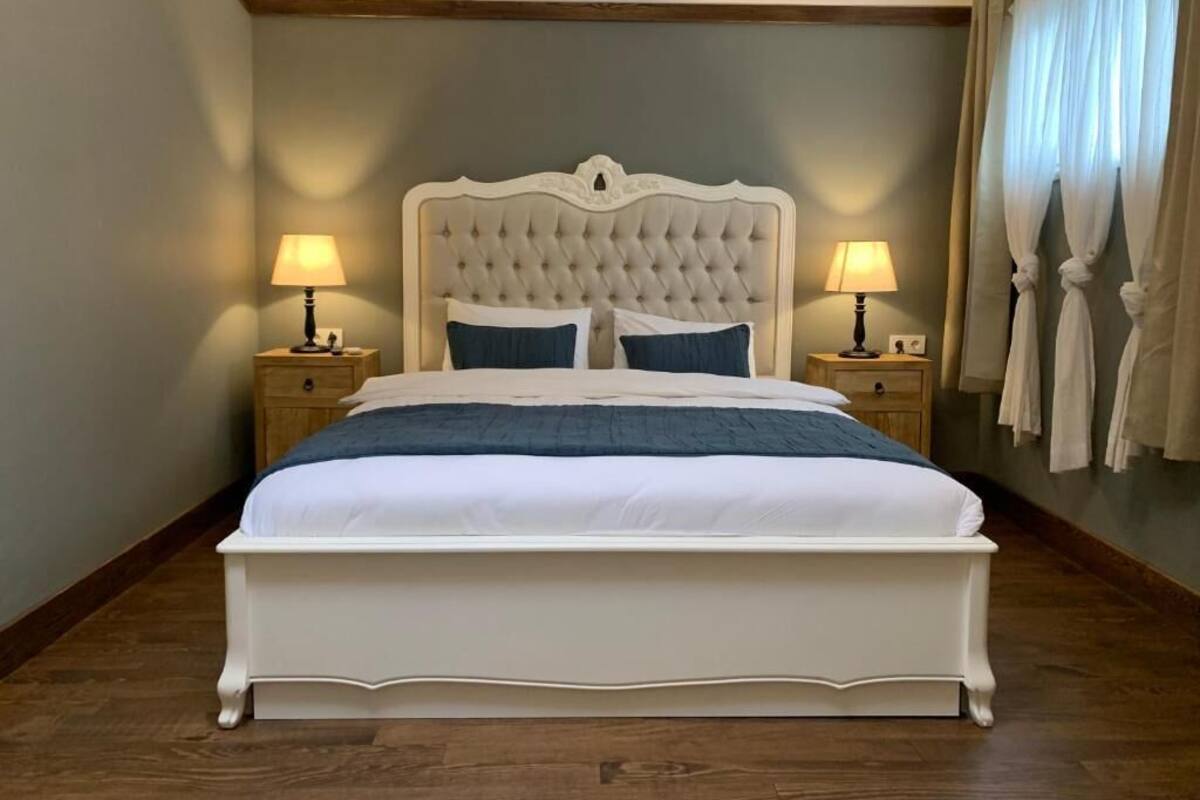 Un letto grande con testiera trapuntata, due lampade ai lati del letto e vista del pavimento in legno della stanza.