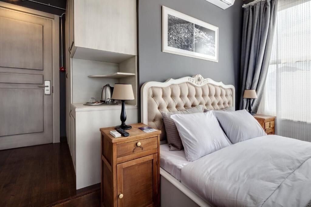 A hotel room with a bed, bedside tables, a wardrobe, a desk with a lamp, and a framed picture on the wall.