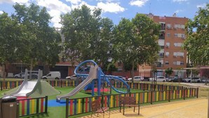A playground with slides and swings, surrounded by a fence and benches. - Palacio Congresos - Airport (Sevilla)