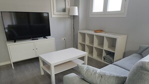 A living room with a TV, white furniture, a grey sofa, and a lamp. - Palacio Congresos - Airport (Sevilla)