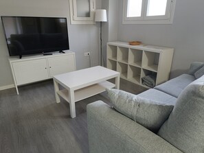 A living room with a TV, white furniture, a grey sofa, and a lamp. - Palacio Congresos - Airport (Sevilla)
