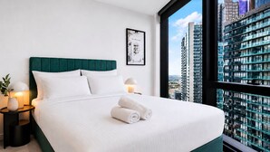 A modern hotel room with a large bed, a city view, a framed picture on the wall, and a nightstand with a lamp. - Skyline 2-bed Near Crown With Pool and Sauna (Melbourne)