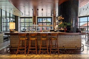 Eine Bar mit einer hohen Theke, vier Hockstühlen und einem großen Fenster.