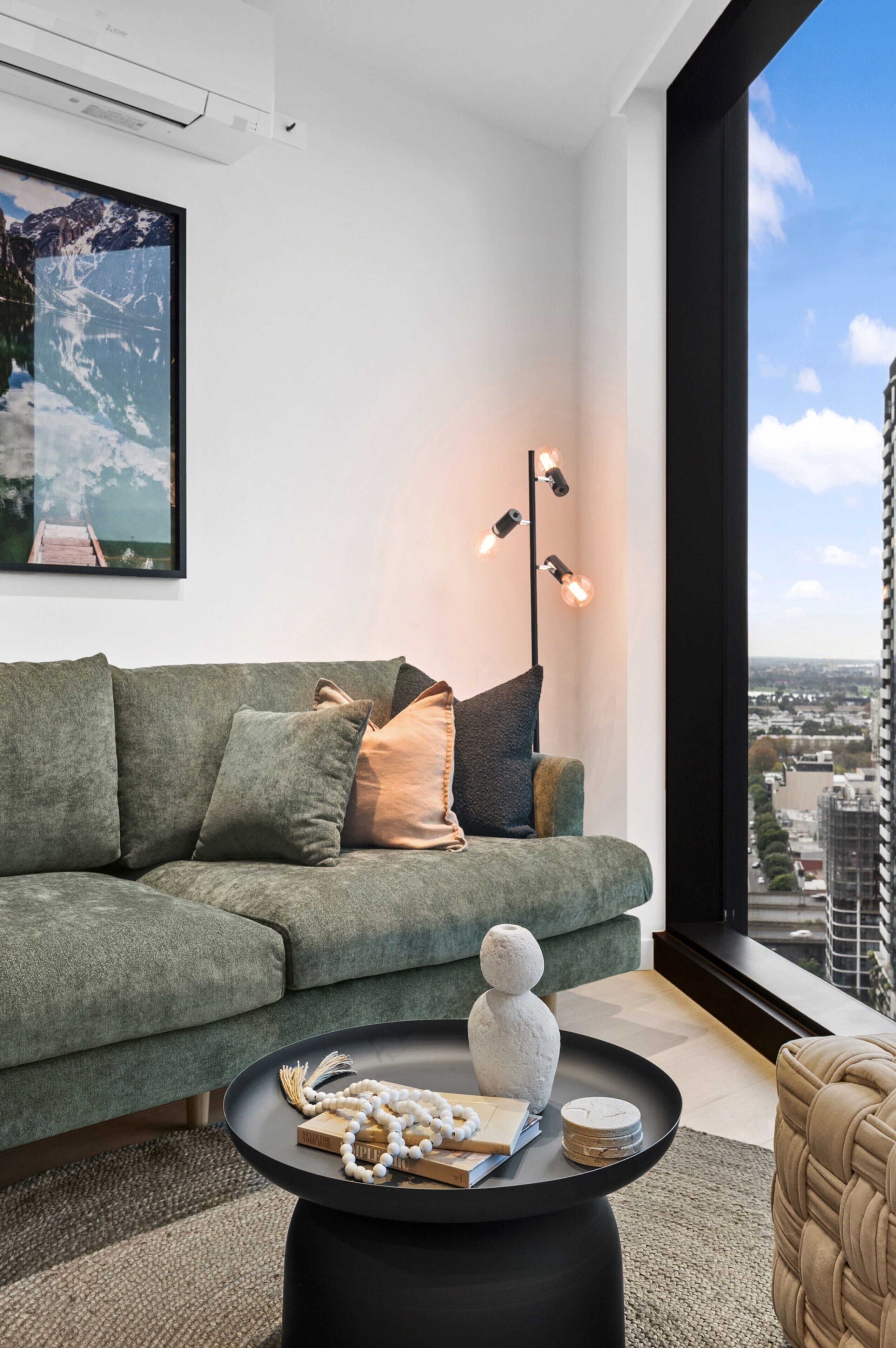 Ein modernes Wohnzimmer mit einem grünen Sofa, einem schwarzen Couchtisch und Blick auf die Stadt durch ein großes Fenster.
