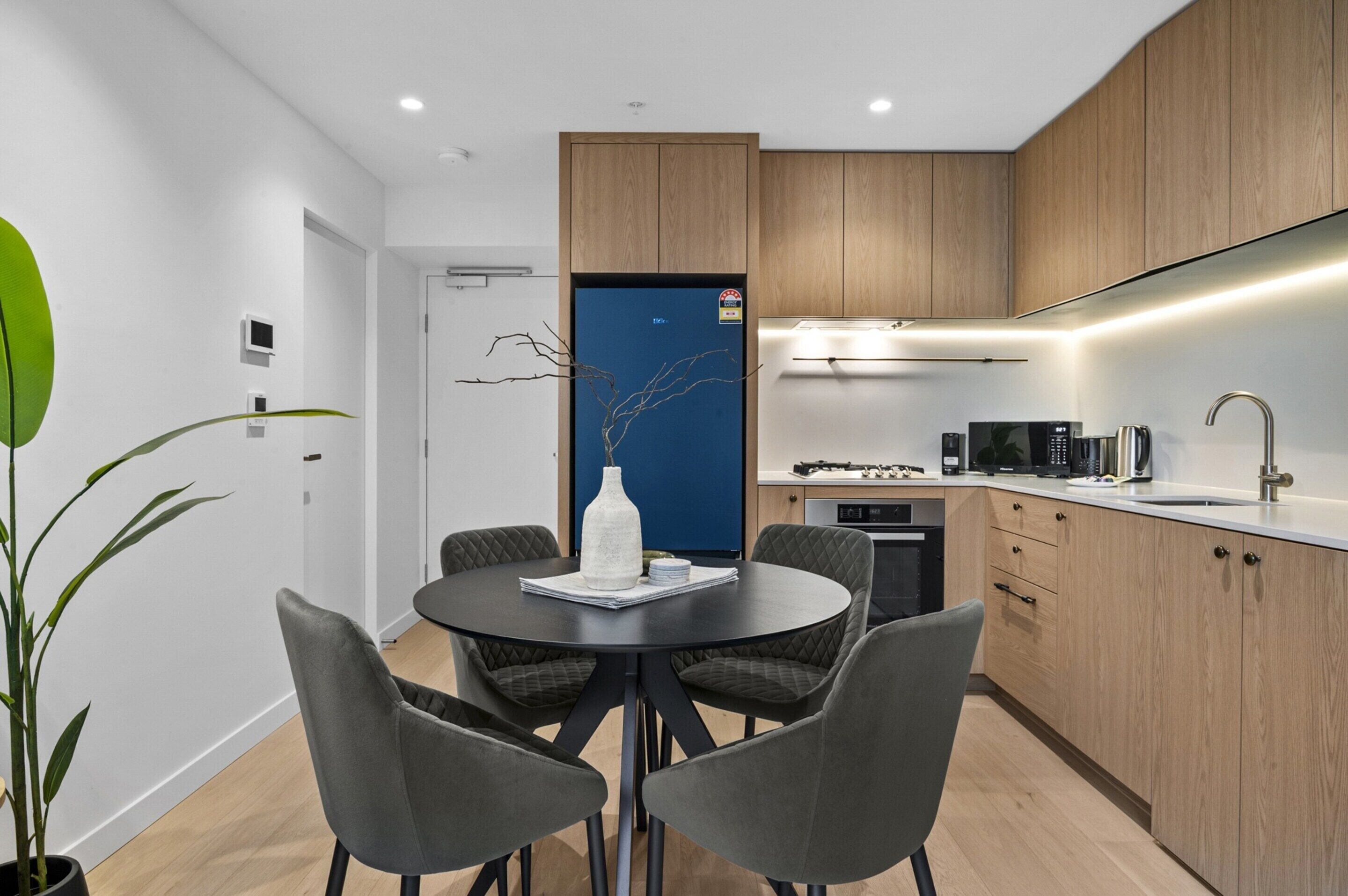 A modern kitchen with wooden cabinets, a built-in microwave, and a dining area with a round table and chairs.