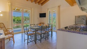Ein Essbereich mit Tisch und Stühlen, eine Küche mit Herd und ein an der Wand befestigter Fernseher.