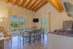 Ein Essbereich mit Tisch und Stühlen, eine Küche mit Herd und ein an der Wand befestigter Fernseher.