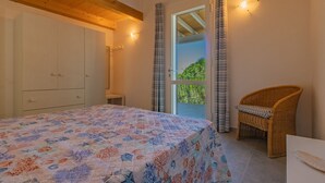 Un dormitorio con cama, una silla de mimbre, un armario y una puerta que da a un balcón.
