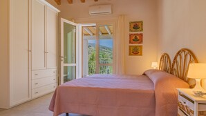 A bedroom with a bed, a wardrobe, a bedside table with a lamp, and a balcony with a view. - Villa Artistica - Villa Artistica - Rosso (Capoliveri)