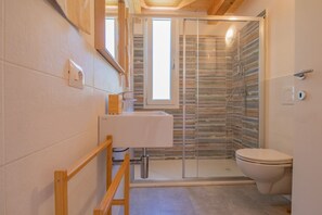 Un baño moderno con cabina de ducha de vidrio, un lavamanos blanco y un inodoro.