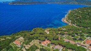 An aerial view of a coastal area with houses, a clear blue sea, and a mountainous backdrop. - Villa Artistica - Villa Artistica - Rosso (Capoliveri)
