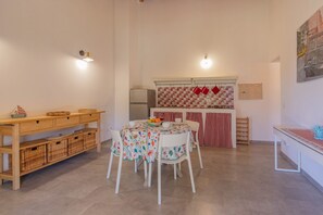 Comedor con una mesa lista para dos personas, un aparador de madera y una zona de cocina con refrigerador y estufa.
