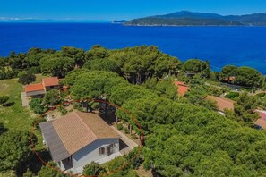 Zona residencial con casas rodeadas de árboles, un mar azul cristalino y montañas al fondo.