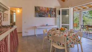 A kitchen with a dining area, a painting on the wall, and a view of greenery outside. - Villa Artistica - Villa Artistica - Rosso (Capoliveri)