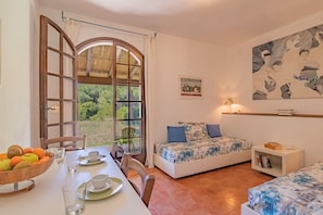 A room with a bed, a table with fruit and cups, a window with curtains, and a painting on the wall. - Villa Valentina - Villa Valentina 1 (Capoliveri)