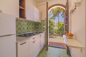 Une cuisine étroite avec une cuisinière à gaz, des placards blancs et un dosseret de carrelage vert.