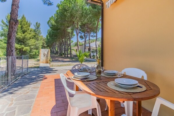 An outdoor dining area with a wooden table, white chairs, and a stone pathway leading to a building. - Villa Valentina - Villa Valentina 2 (Capoliveri)