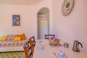Une pièce comprenant un lit, une table à manger avec des chaises, un panier, une théière et une tasse.