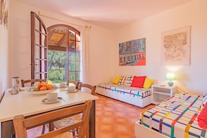 A room with a dining table, two beds, a window with a view of trees, and artwork on the walls. - Villa Valentina - Villa Valentina 3 (Capoliveri)