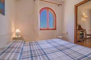 A bedroom with a bed, a window with a red frame, a chair, and a desk. - Villa Valentina - Villa Valentina 4 (Capoliveri)