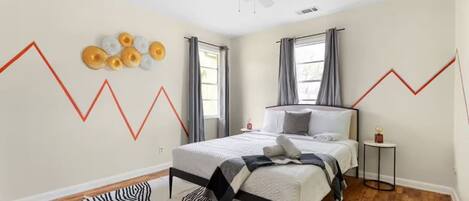 Une chambre à coucher comprenant un lit, un ventilateur de plafond, un tapis à motifs zébrés, une petite table ronde avec un globe terrestre et un mur orné d’un motif en zigzag.