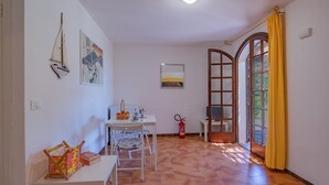 Una habitación con una mesa, sillas, extintor, una ventana con cortinas amarillas y obras de arte en las paredes.