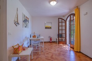 Ein Zimmer mit Tisch, Stühlen, einem Feuerlöscher, einem Fenster mit gelben Vorhängen und Bildern an den Wänden.