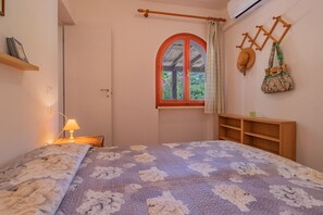 Ein Schlafzimmer mit Bett, Fenster mit Blick, Nachttischlampe und einem an der Wand befestigten Gepäckträger.