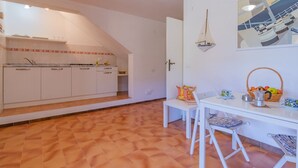 Una cocina con armarios blancos, un comedor con mesa y sillas, y un adorno náutico de un velero colgante.