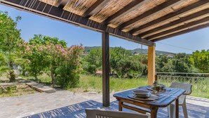 Un patio al aire libre con mesa y sillas, una pérgola encima y vistas a zonas verdes y colinas.