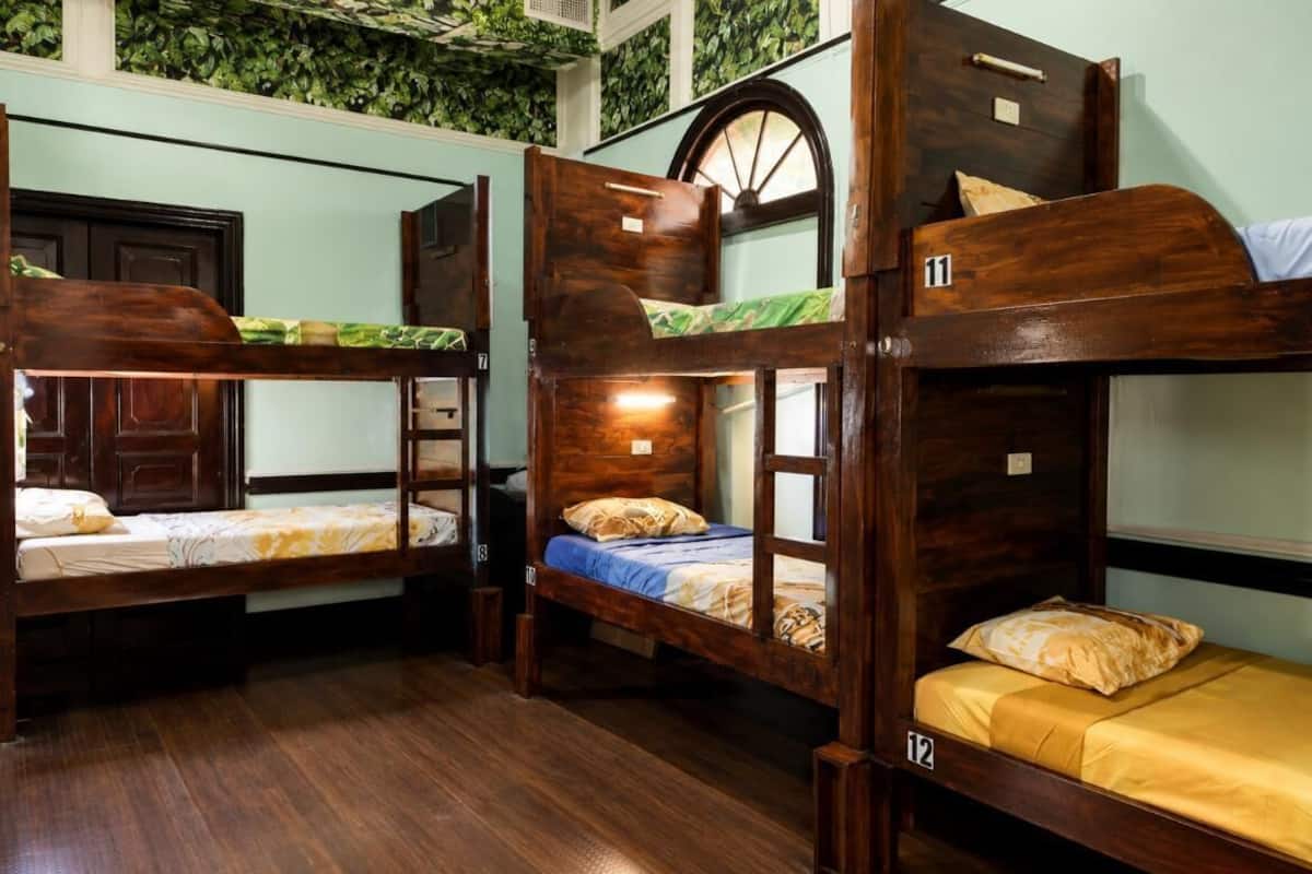 A room with bunk beds, numbered 11 and 12, wooden floors, and a green leafy wall.