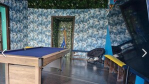 Una mesa de billar, un sofá, un televisor y una puerta con marco verde.