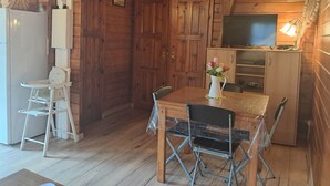A wooden cabin interior with a dining table, chairs, a television, and a refrigerator.